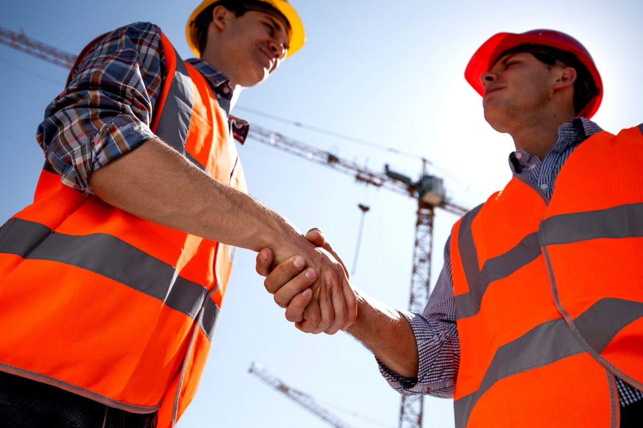 Structual engineer and architect dressed in orange work vests and helmets shake hands